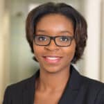 A woman wearing glasses and a black blazer, likely a manufacturer representative, smiles at the camera in a well-lit, blurred indoor setting—perfectly suited for discussions on EUDAMED compliance or medical devices.