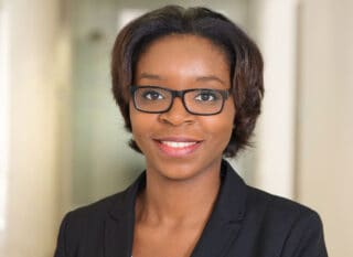 A woman wearing glasses and a black blazer, likely a manufacturer representative, smiles at the camera in a well-lit, blurred indoor setting—perfectly suited for discussions on EUDAMED compliance or medical devices.